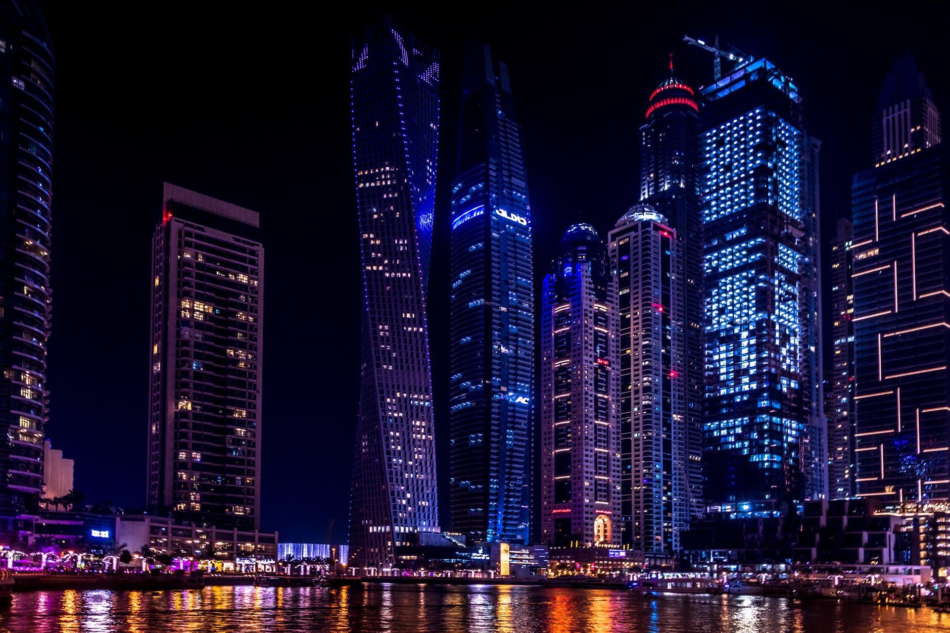 Nighttime city skyline with illuminated blue and pink skyscrapers reflecting on water