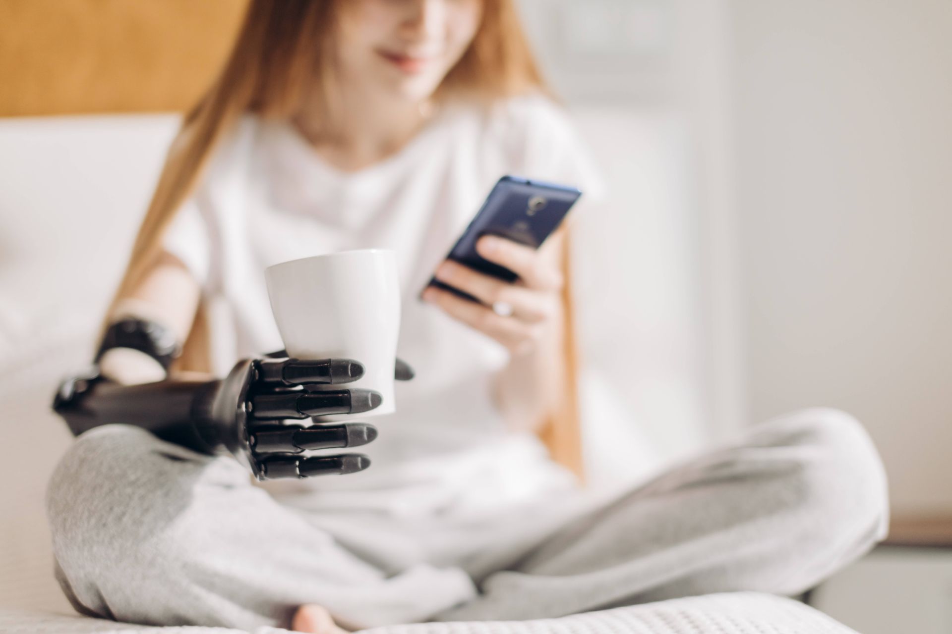 Woman with a prosthetic arm holding a cup of coffee while scrolling her phone at Durrett's Orthotic & Prosthetic near Edgewood, KY, and Lawrenceburg, IN