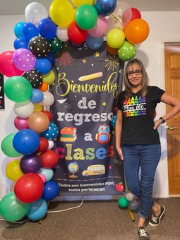 A woman is standing in front of a sign that says bienvenidos de regreso a clases