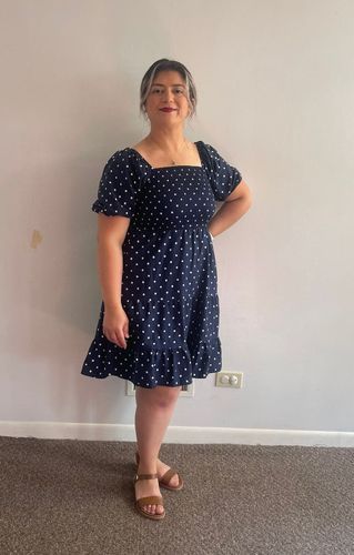 A woman in a blue polka dot dress is standing in a room.