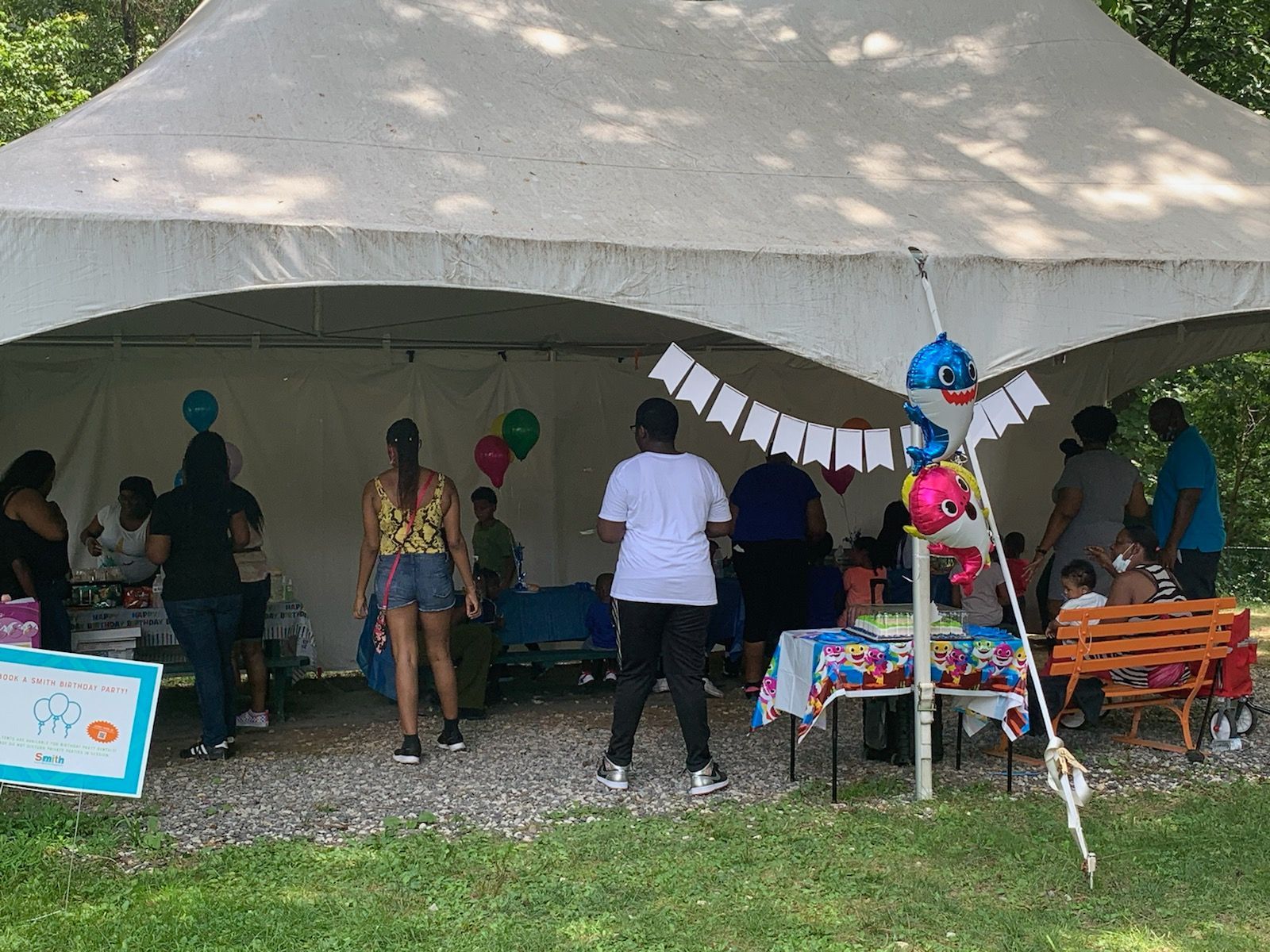 People gathered under a large white tent at an outdoor party with colorful decorations and tables.