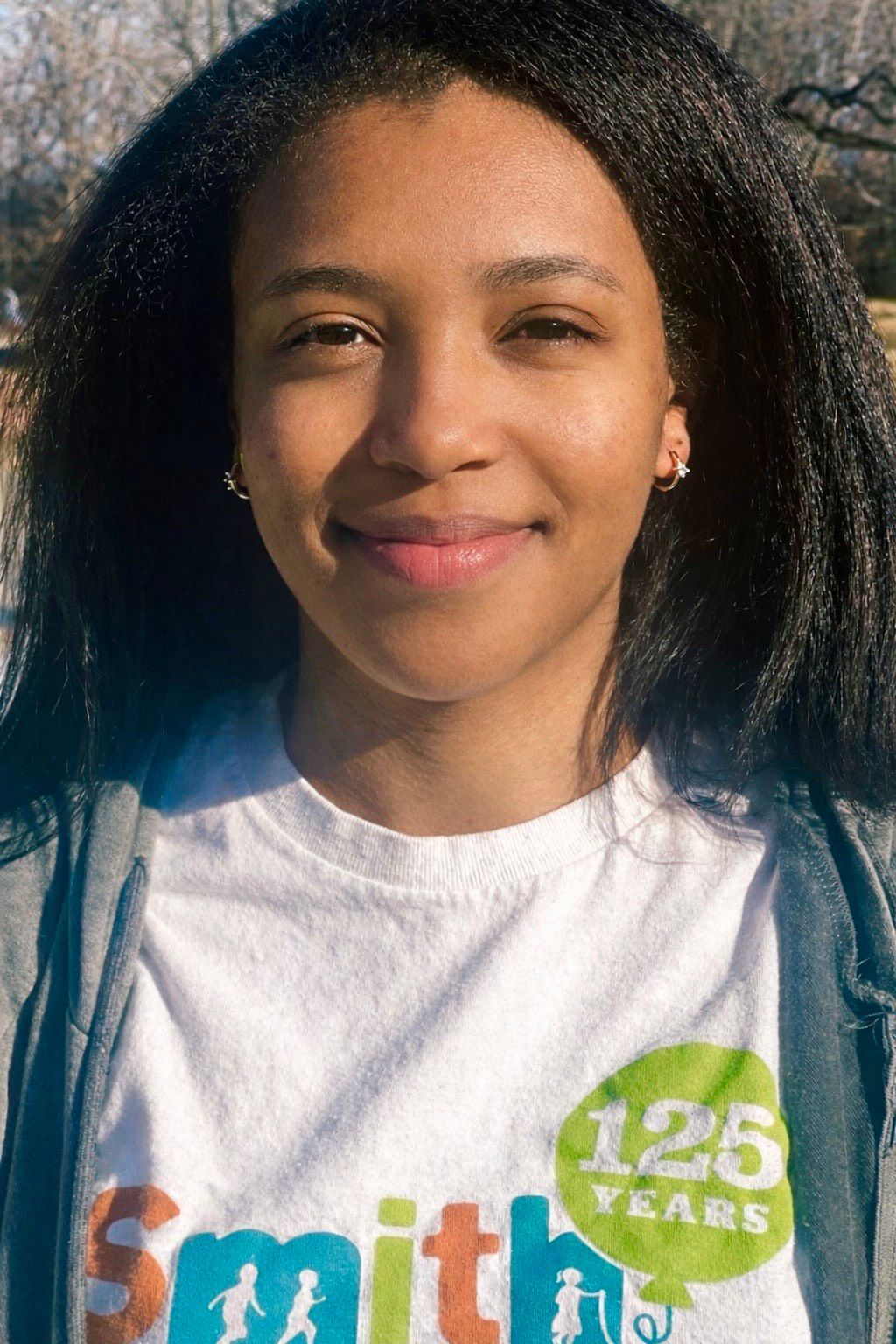 Smiling person outdoors wearing a white Smith T-shirt with a green “125 years” badge