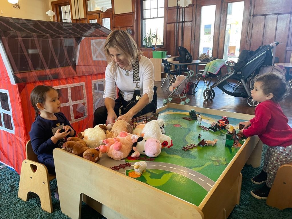Children and an adult play with toys at a small indoor table in a cozy room