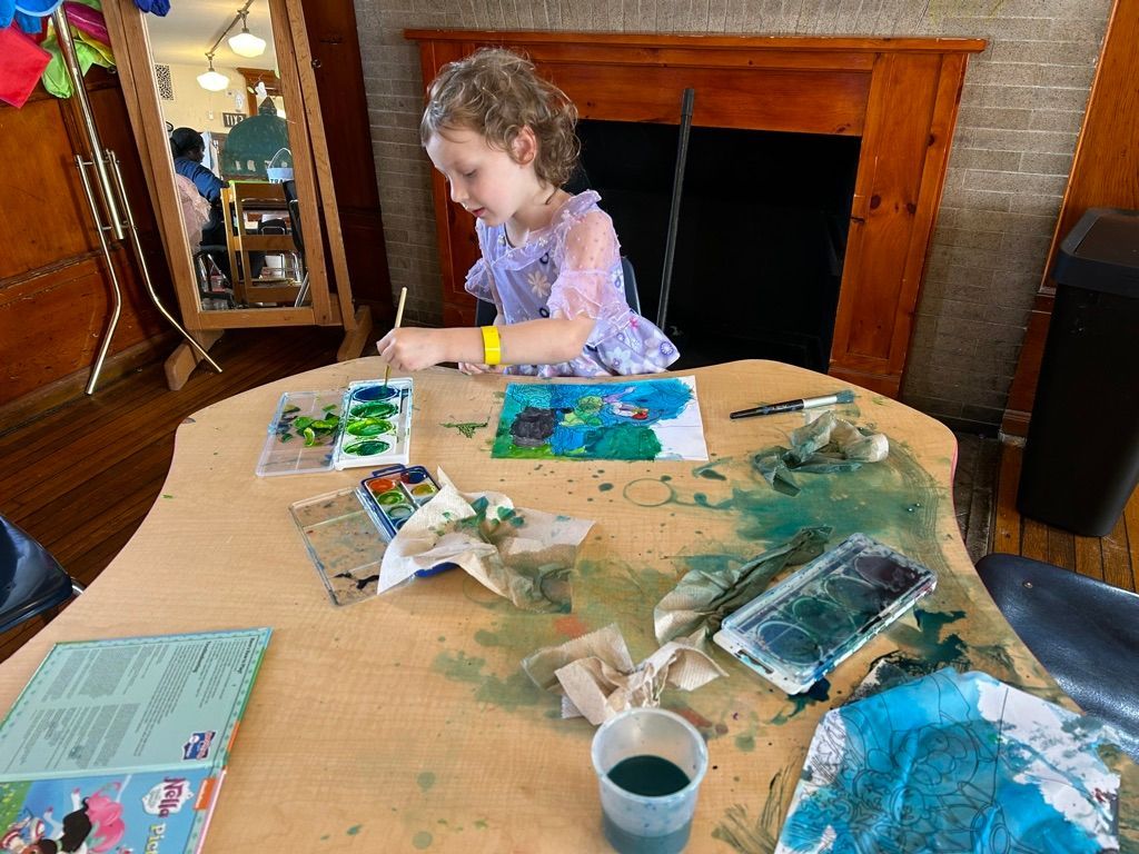 Child painting at a table with art supplies in a living room by a fireplace