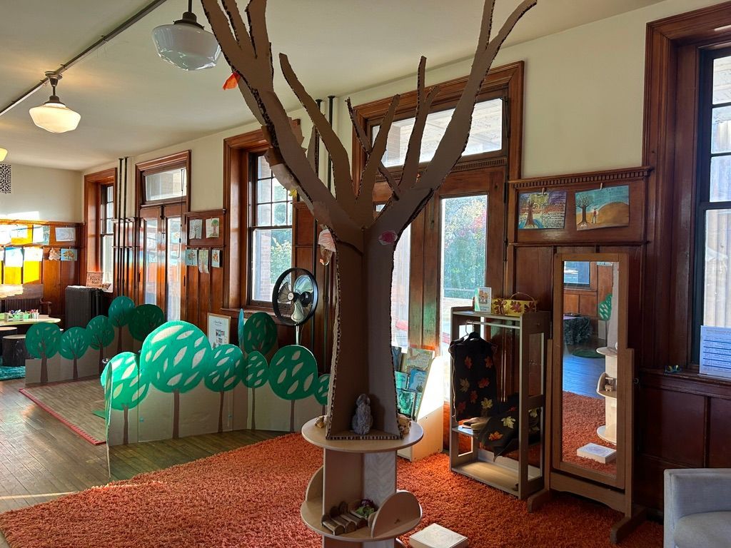 Indoor room with wooden tree sculpture, green chairs, and tall mirrors in a vintage-style space