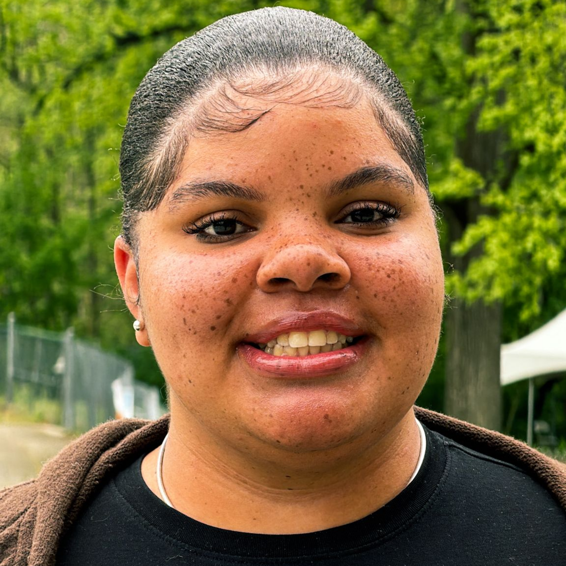 Smiling person in a black shirt outdoors with green trees in the background