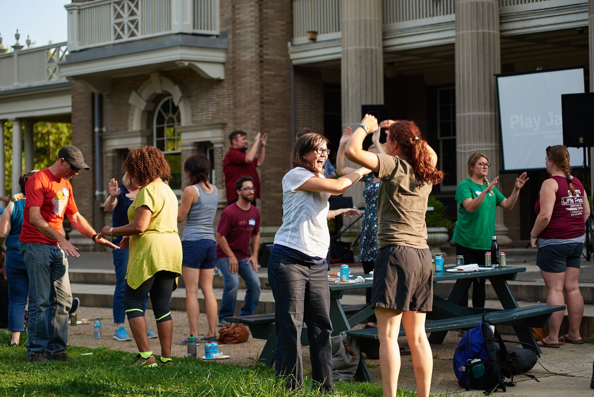 People dancing outdoors in front of a building, with a few others watching nearby.