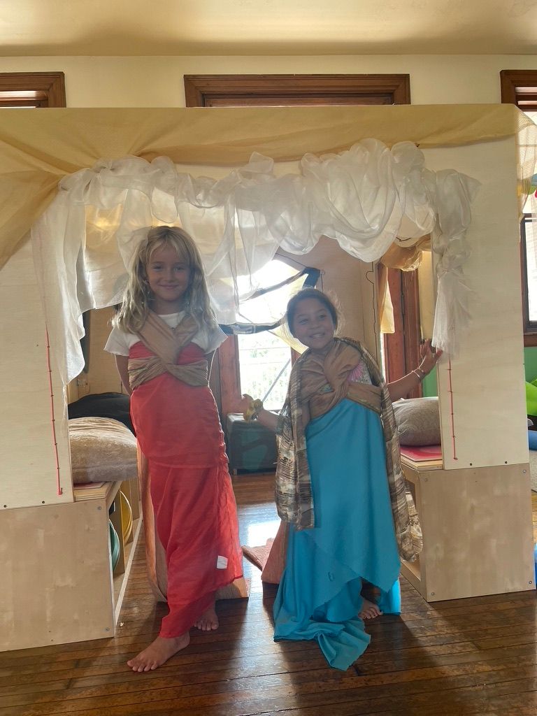 Two children in bright costumes posing under a white draped canopy indoors