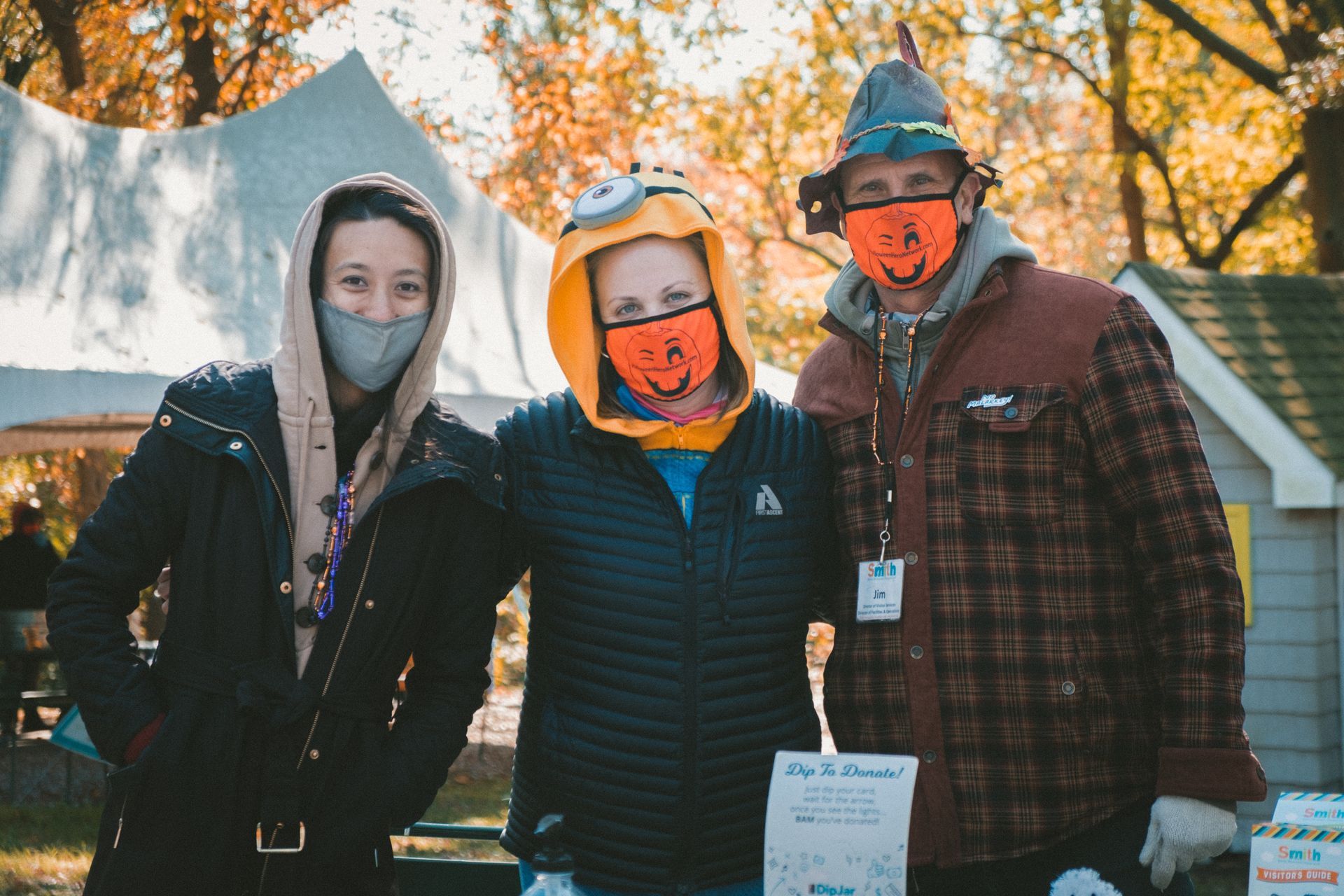 Three bundled-up people posing outdoors at a fall event, wearing face masks and hats.