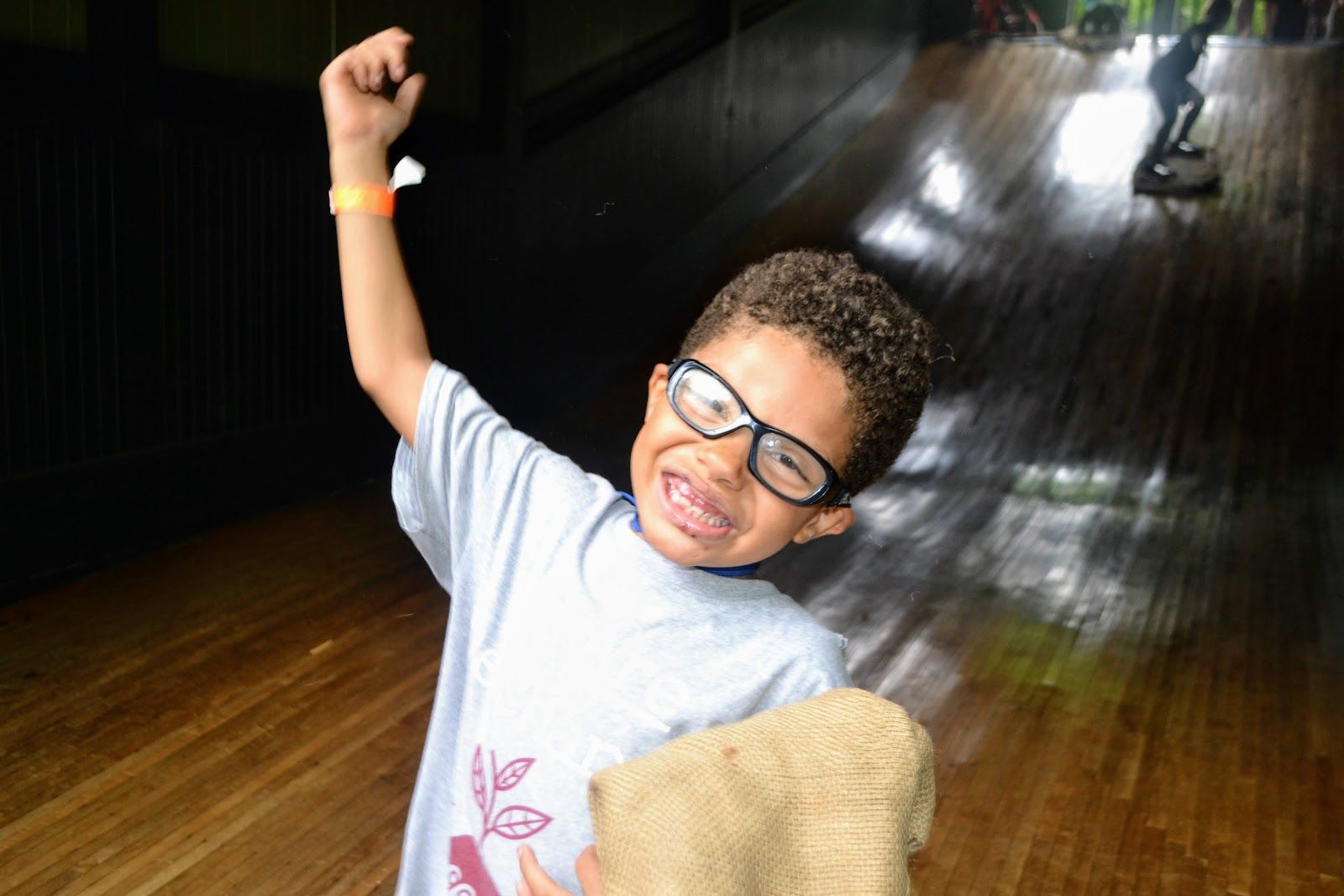 Child smiling with raised fist on an indoor slide, wearing glasses and a light shirt