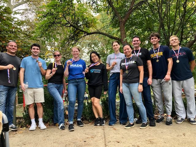 Group of people posing outdoors on a dirt path under trees, smiling at the camera.