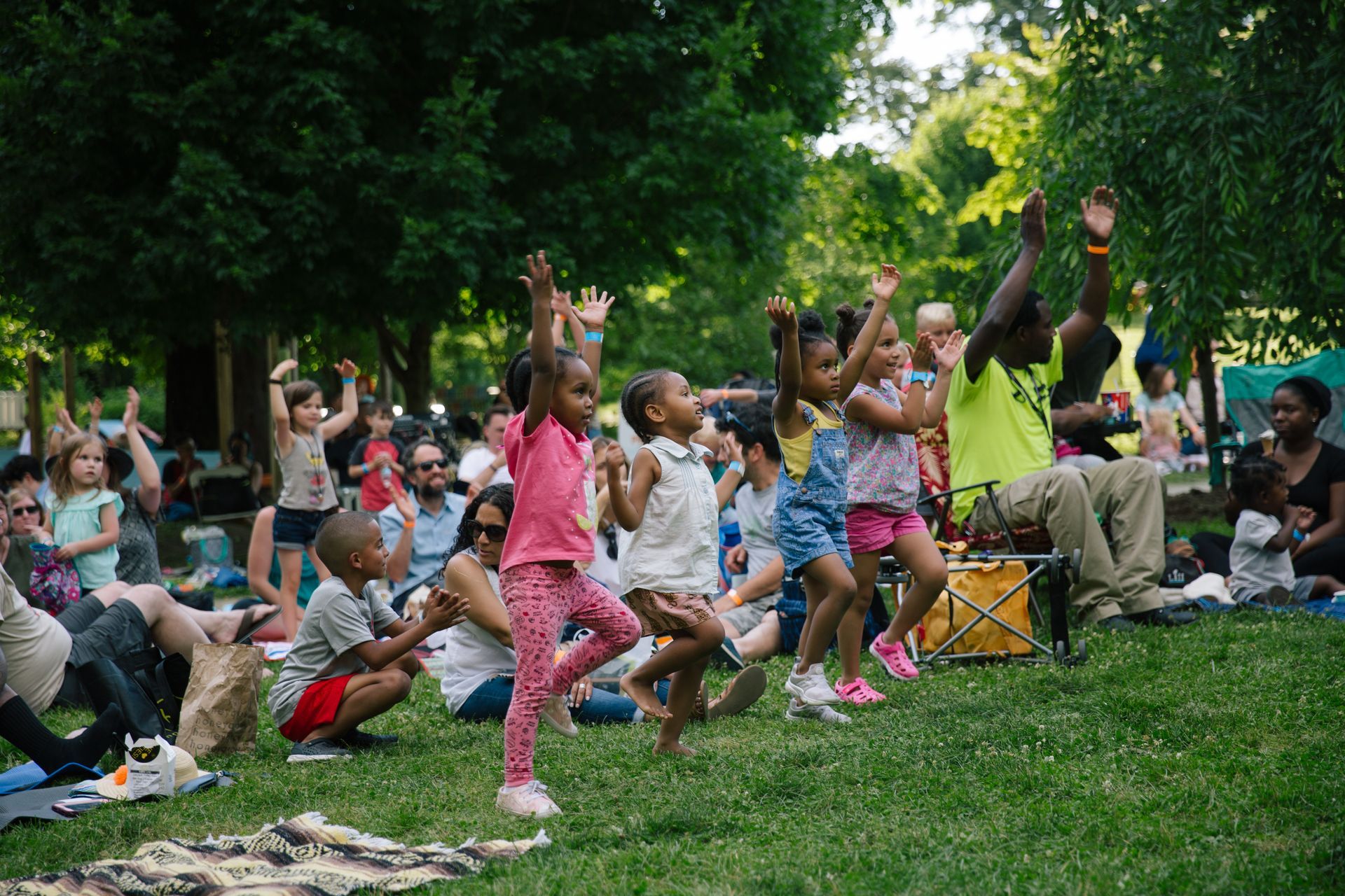 Children and adults cheering with raised hands in a grassy park during a group outdoor event