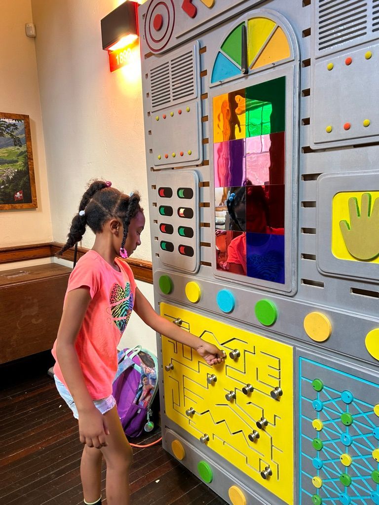 Girl reaching toward a colorful interactive wall panel in a play area.