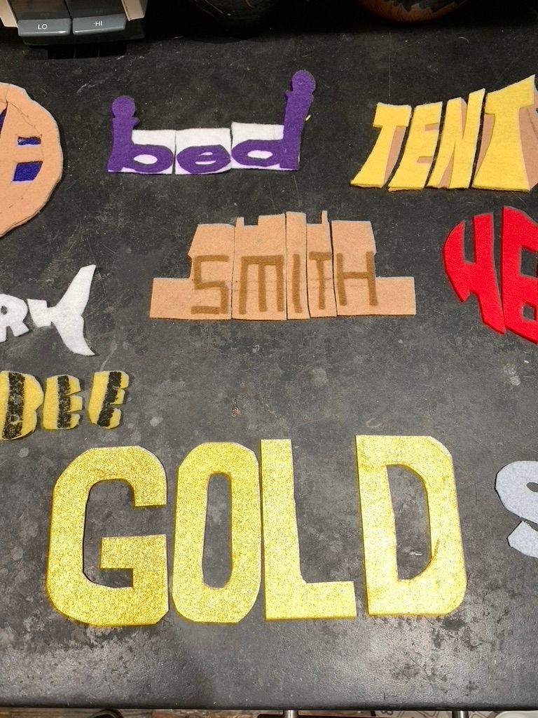 Colorful hand-cut words spelling “GOLD,” “smash,” “bed,” and “TEN” on dark pavement