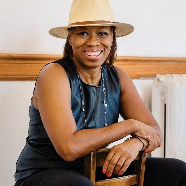 Smiling person in a straw hat leaning on a chair in a bright indoor room