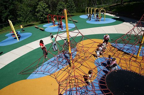 Children playing on a colorful rope playground with climbing nets and swings outdoors