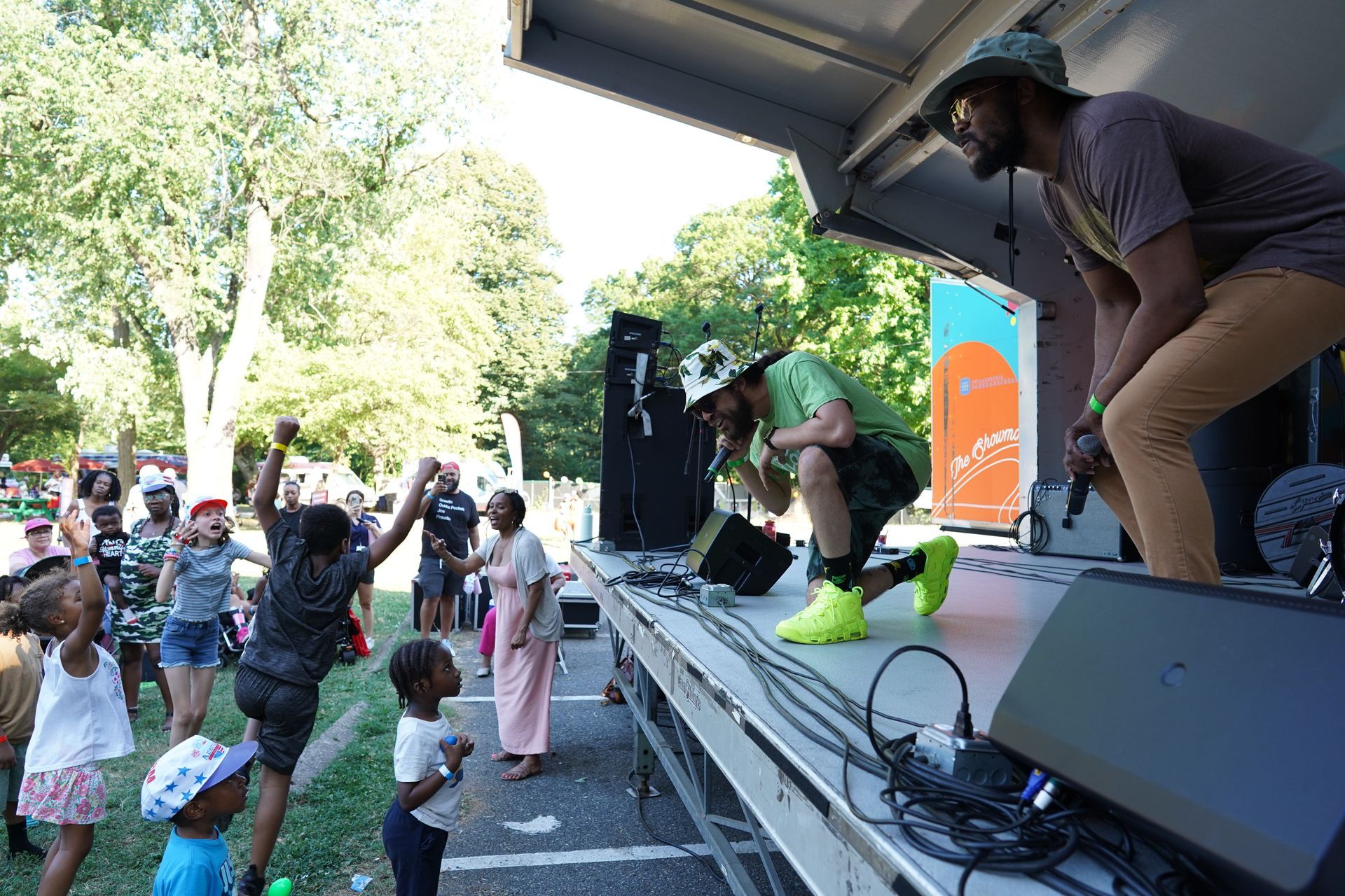 Outdoor stage performance with a singer leaning toward the crowd, children watching from the front.