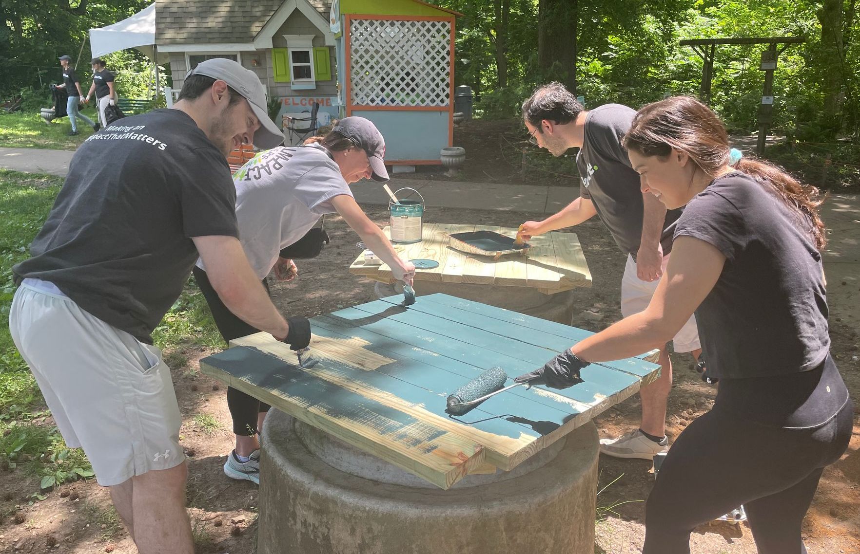 People working together to sand a large blue surface outdoors around a wooden table.