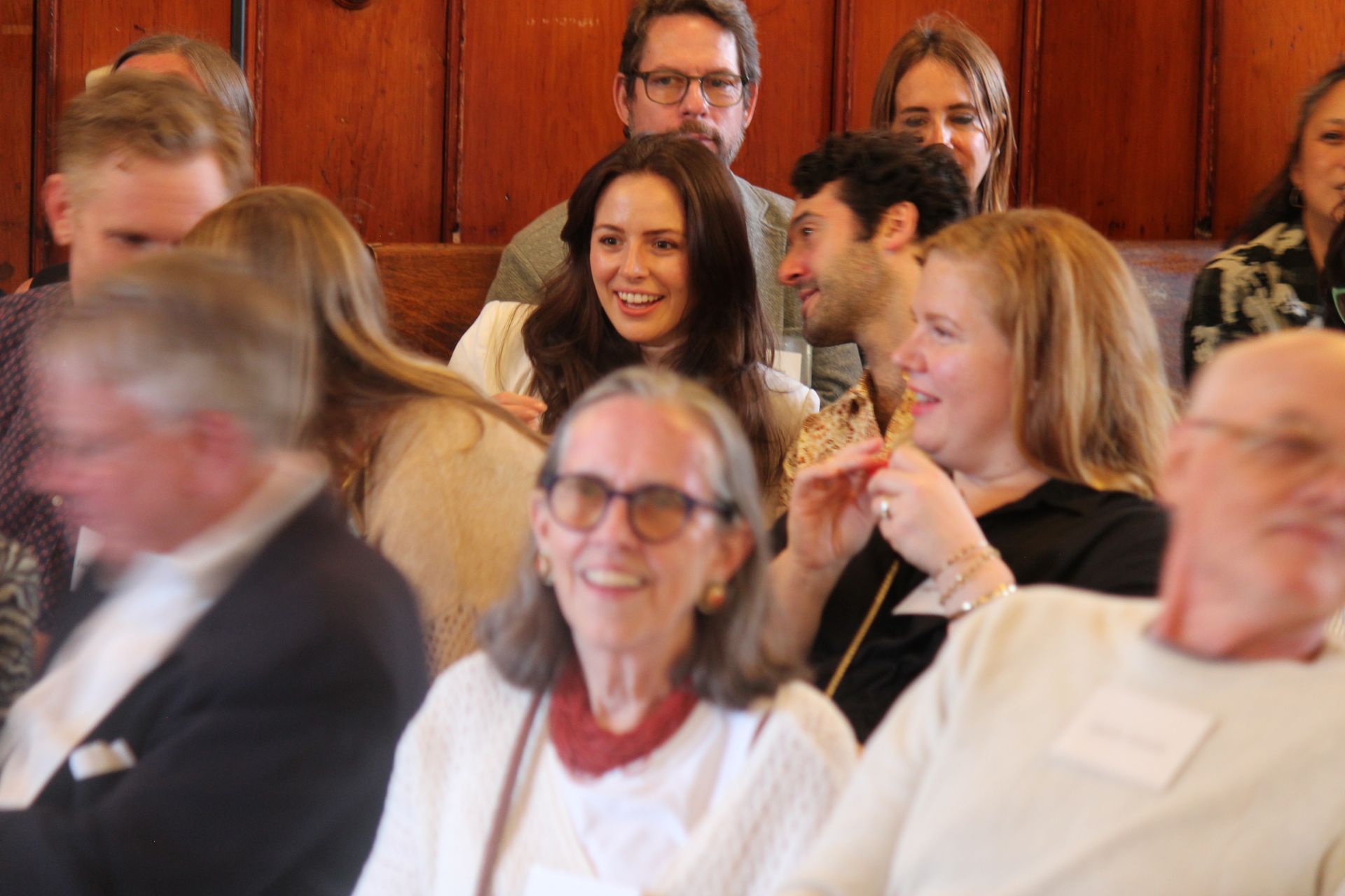 Audience seated in a hall, smiling and talking during a presentation