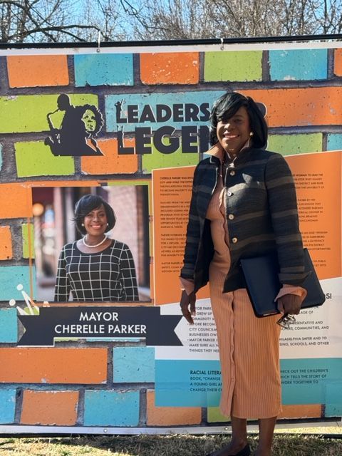Woman smiling beside a colorful mural honoring Mayor Cherelle Parker and leaders