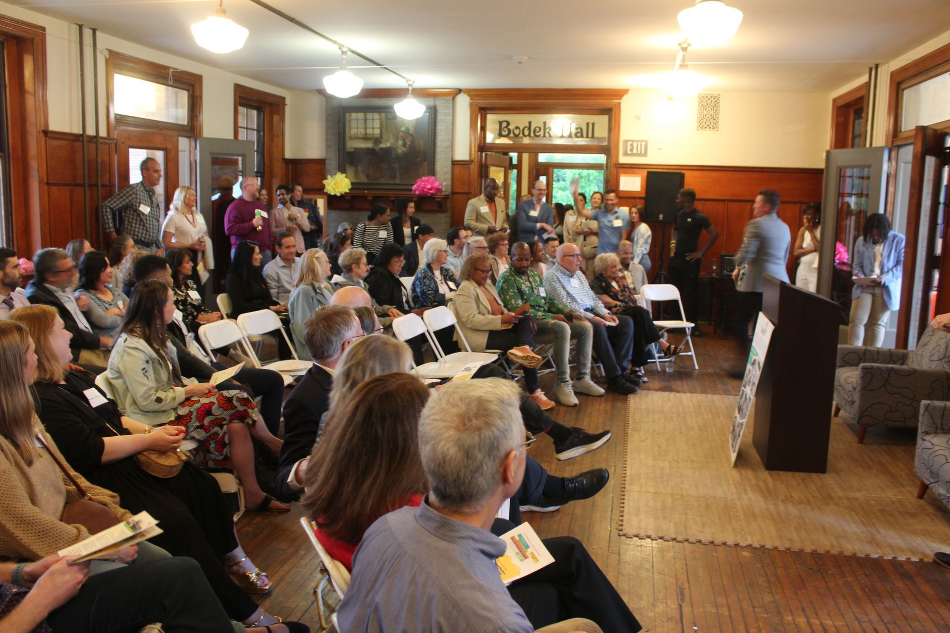 Audience seated in a cozy hall, watching a speaker at the front.