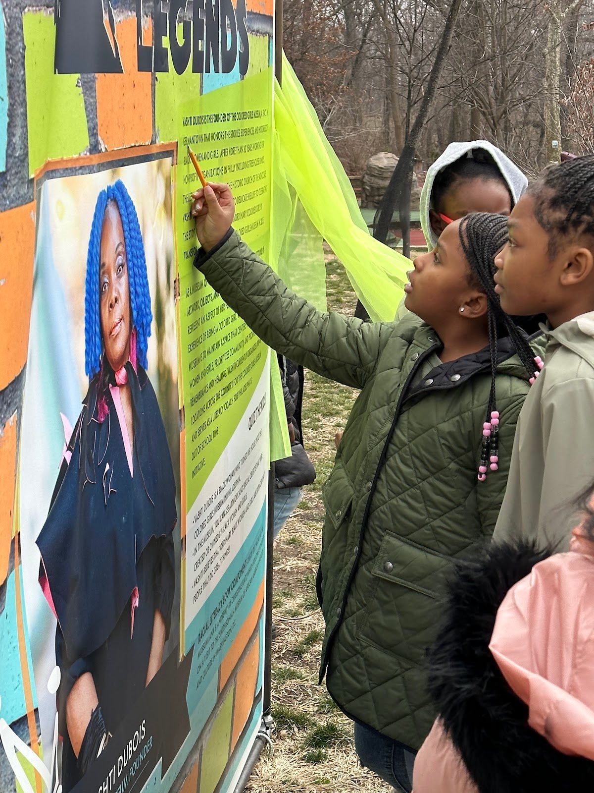 Children looking at a colorful outdoor poster, with one pointing at a photo and text on the display