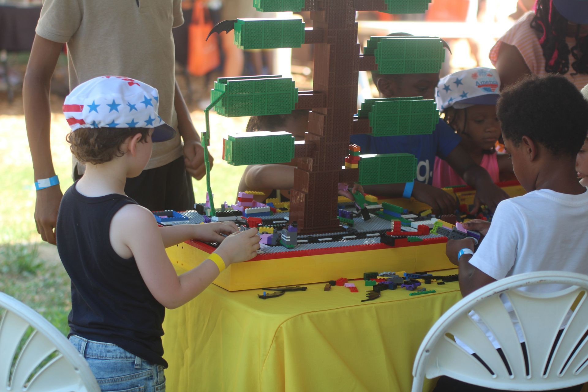 Children playing a colorful carnival game at a table with green shelves and chairs outdoors