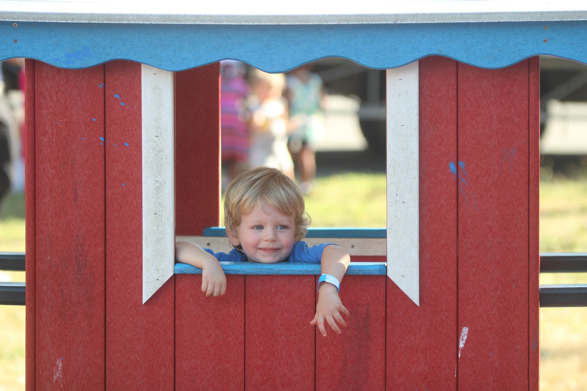 Child peeking through a red wooden fence window, smiling outdoors