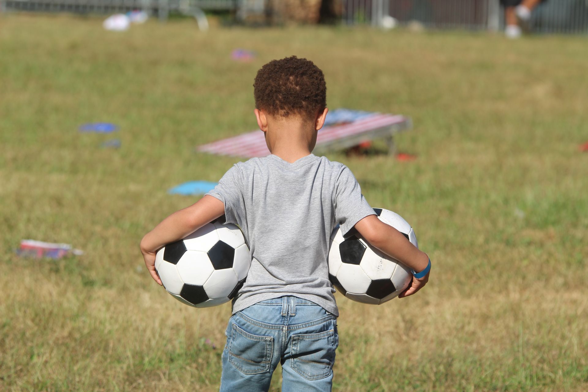Child holding two soccer balls in a grassy field with cones in the background