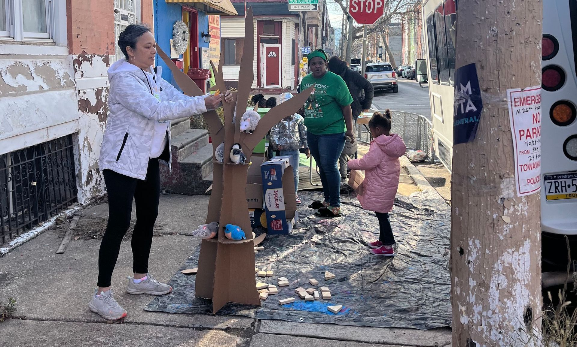 People helping a child on a debris-strewn street beside damaged buildings