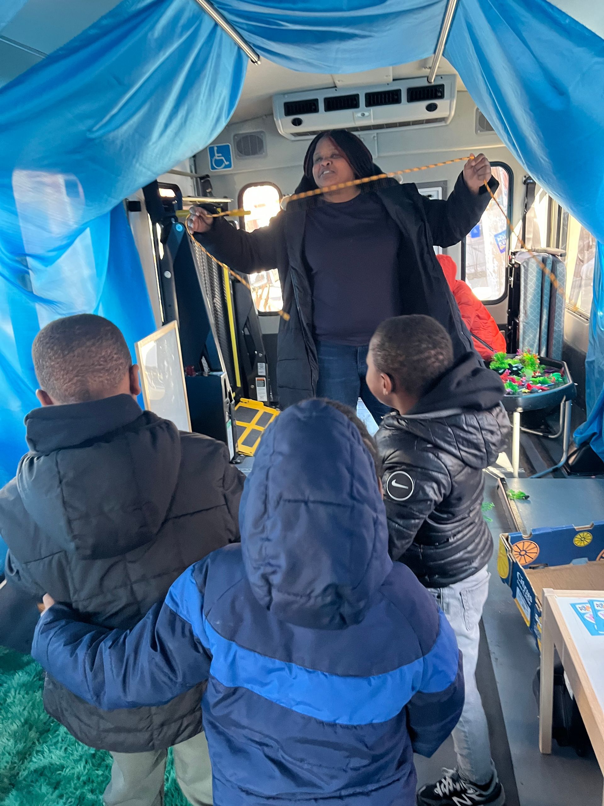 Speaker addressing seated passengers on a bus under a blue canopy