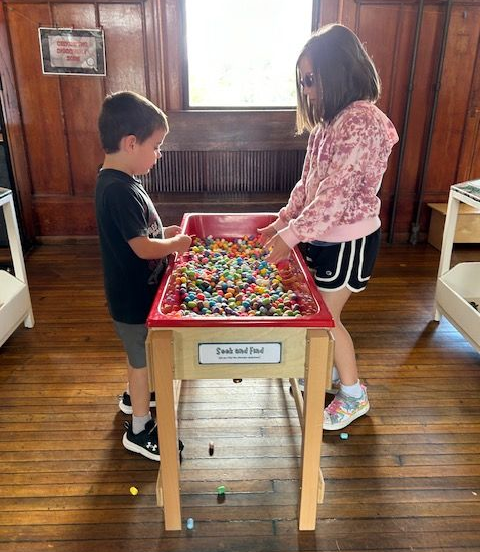 Two children playing a colorful bead maze game in a wooden room