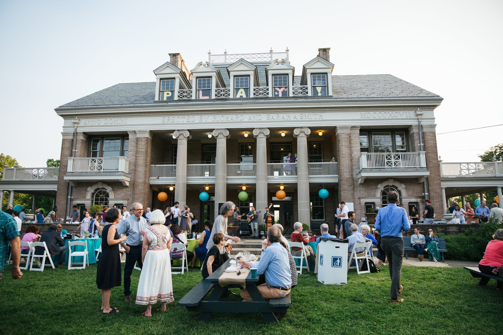 Crowd gathered on a lawn outside a large historic building during an outdoor event