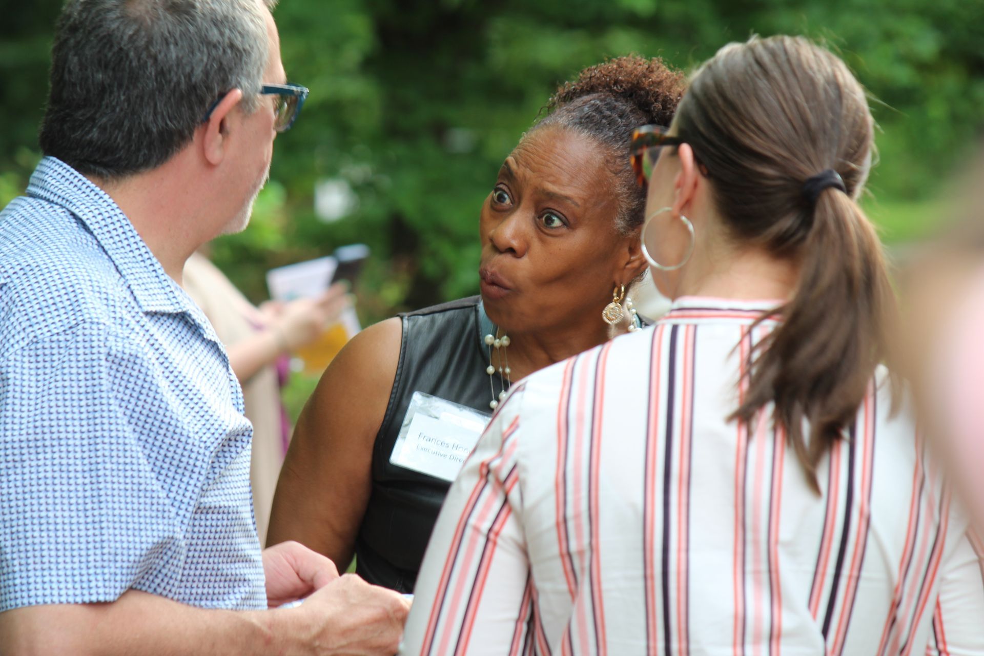 Three people talking outdoors, with one woman gesturing during a conversation.