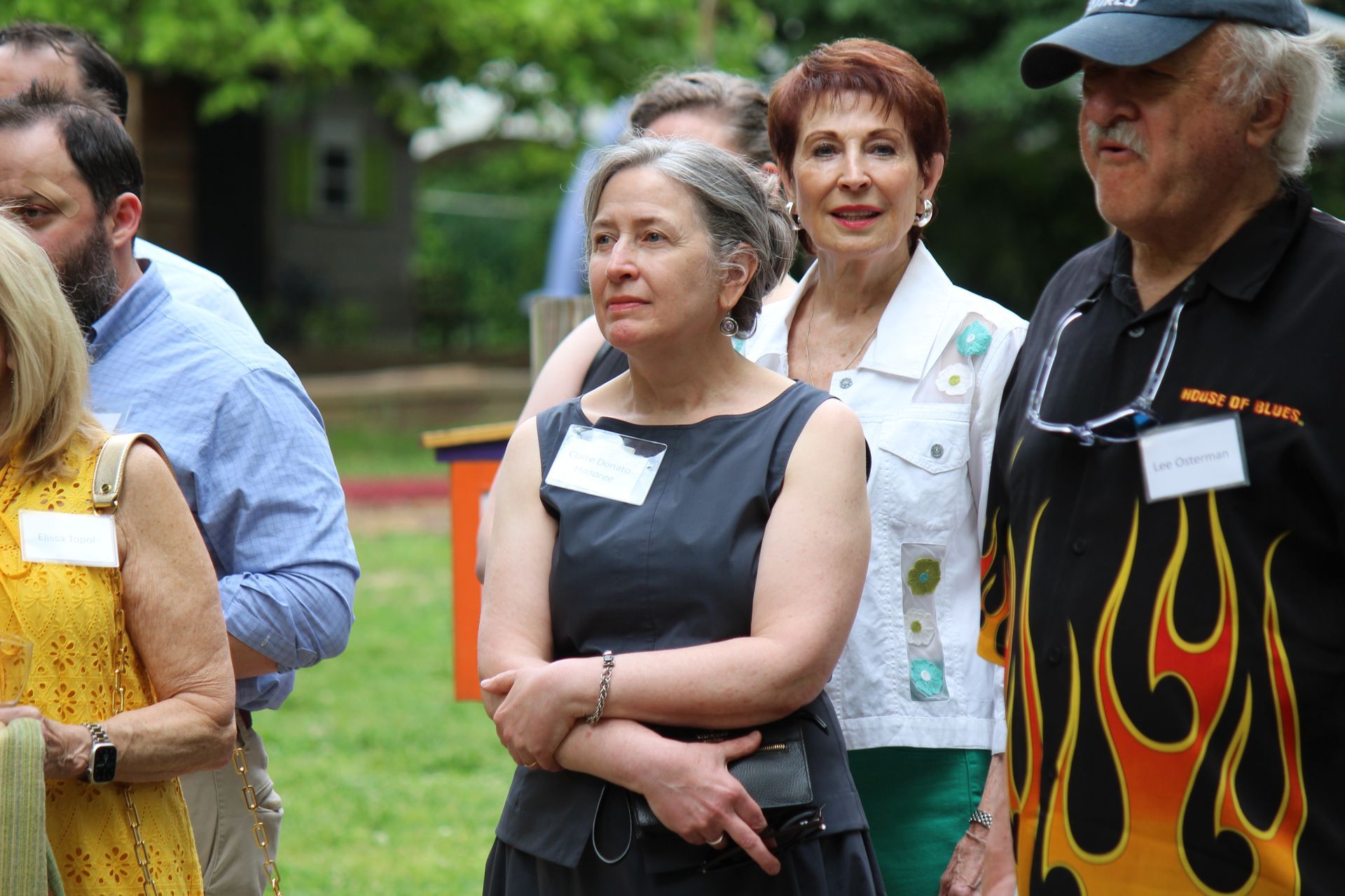 People standing outdoors at a gathering, with one woman in a black top in the foreground.