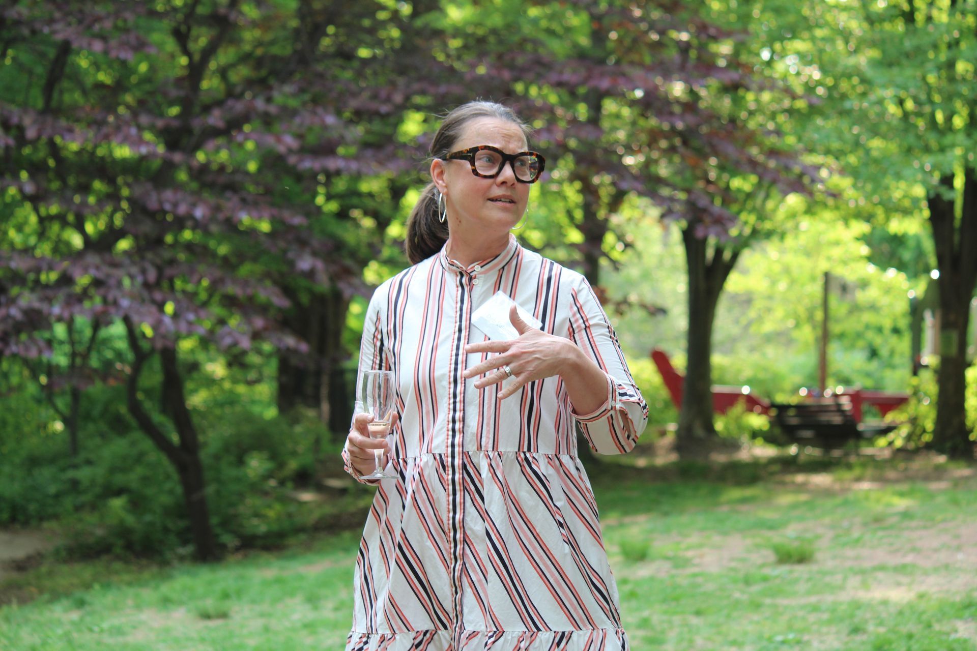 Person in glasses and patterned shirt stands in a green park with trees.