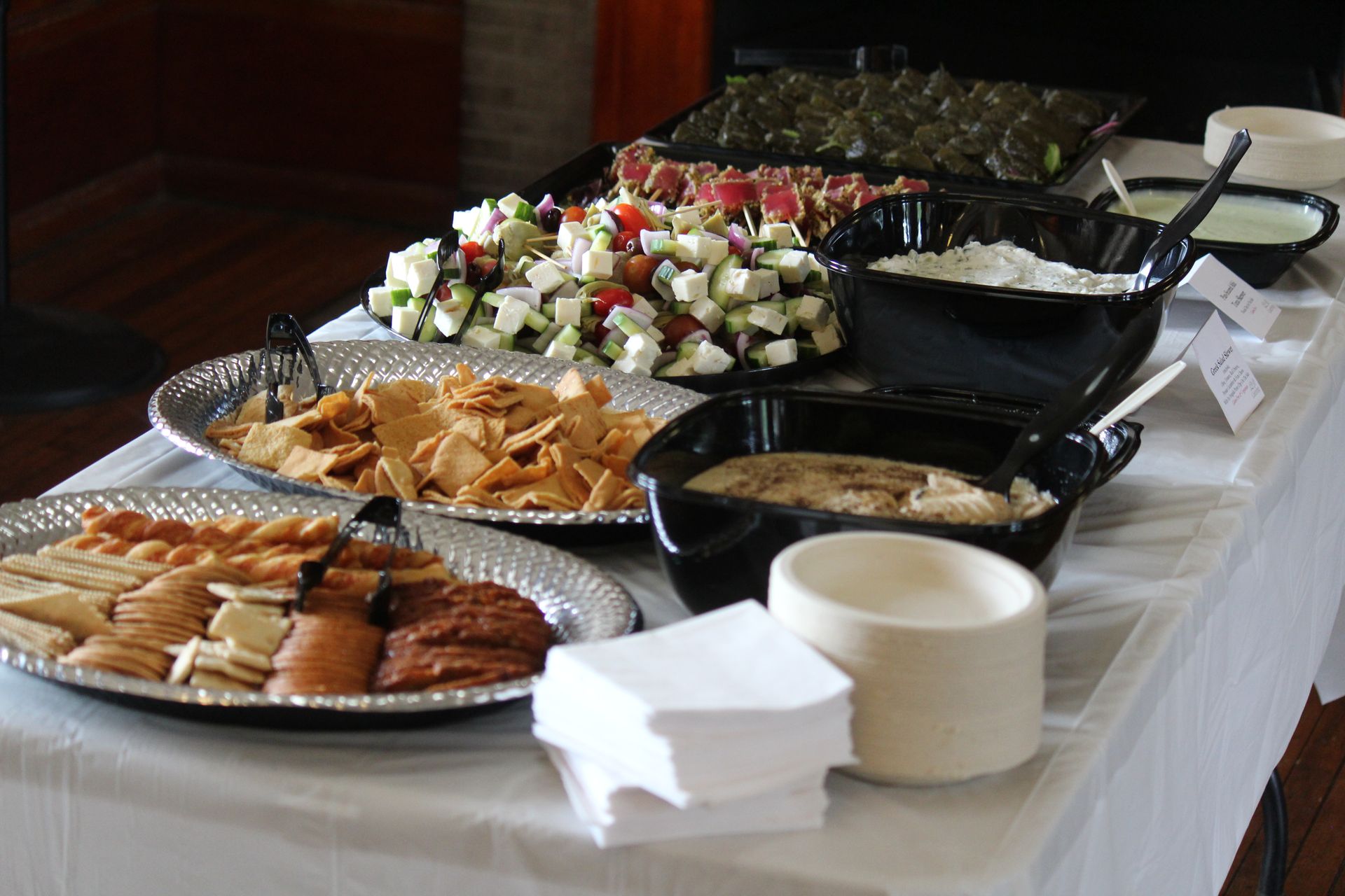Buffet table with assorted appetizers, skewers, pastries, and serving dishes on a white tablecloth