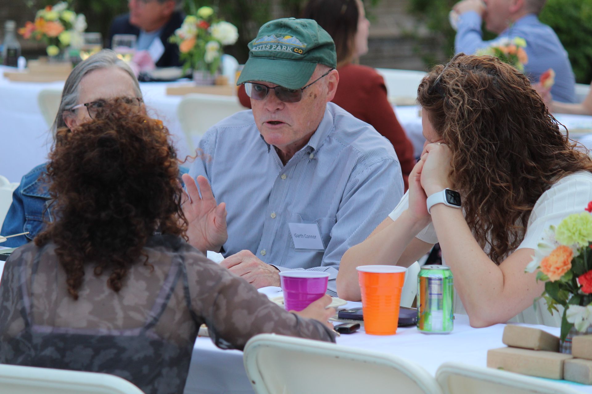 People chatting at an outdoor table with colorful cups and drinks at a café or picnic area