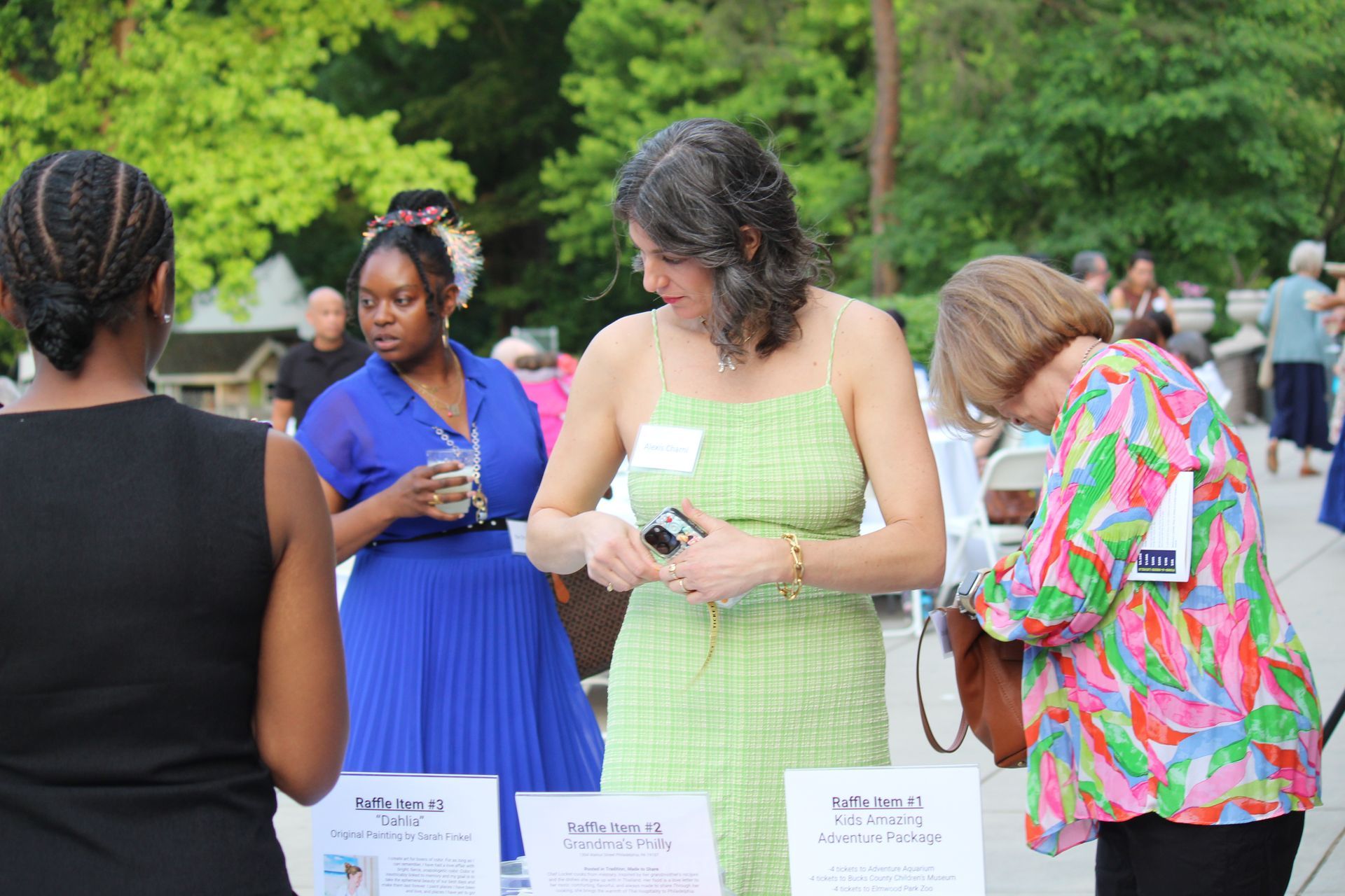 People standing at an outdoor event, reading signs on a table in front of them.