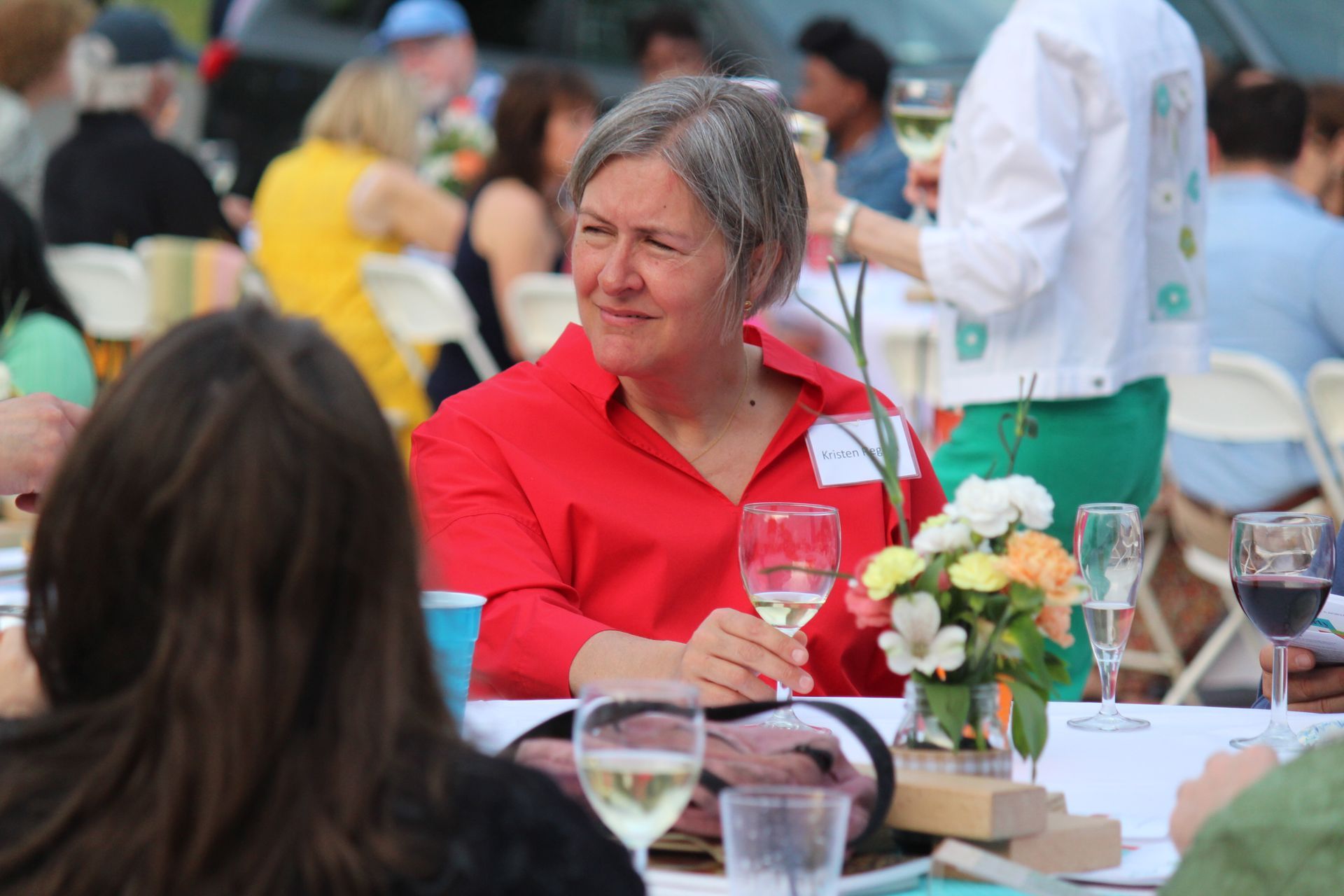 Person in a red jacket seated at an outdoor table with drinks and flowers, looking to the side