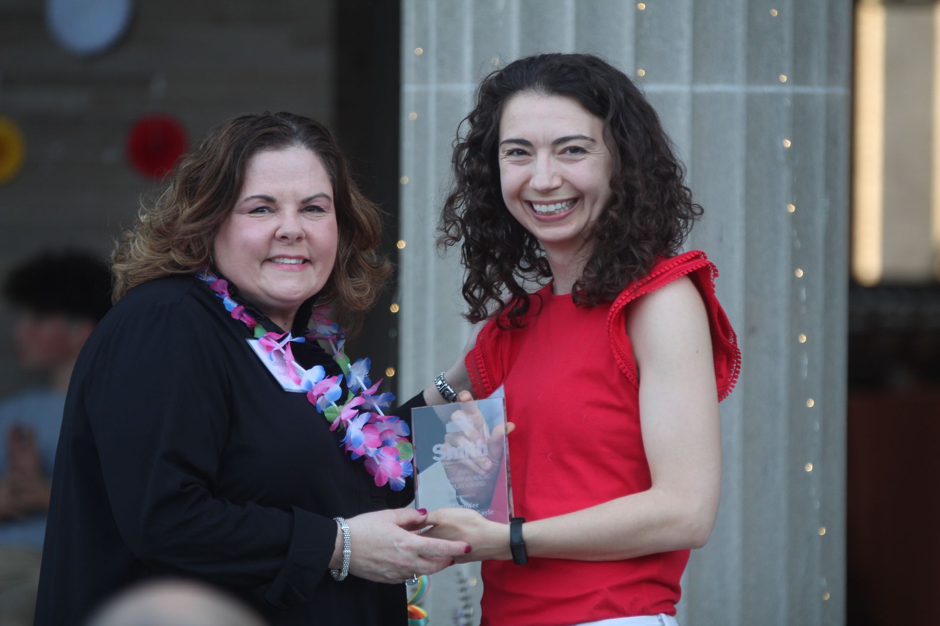 Two women smiling while holding a trophy at an indoor event