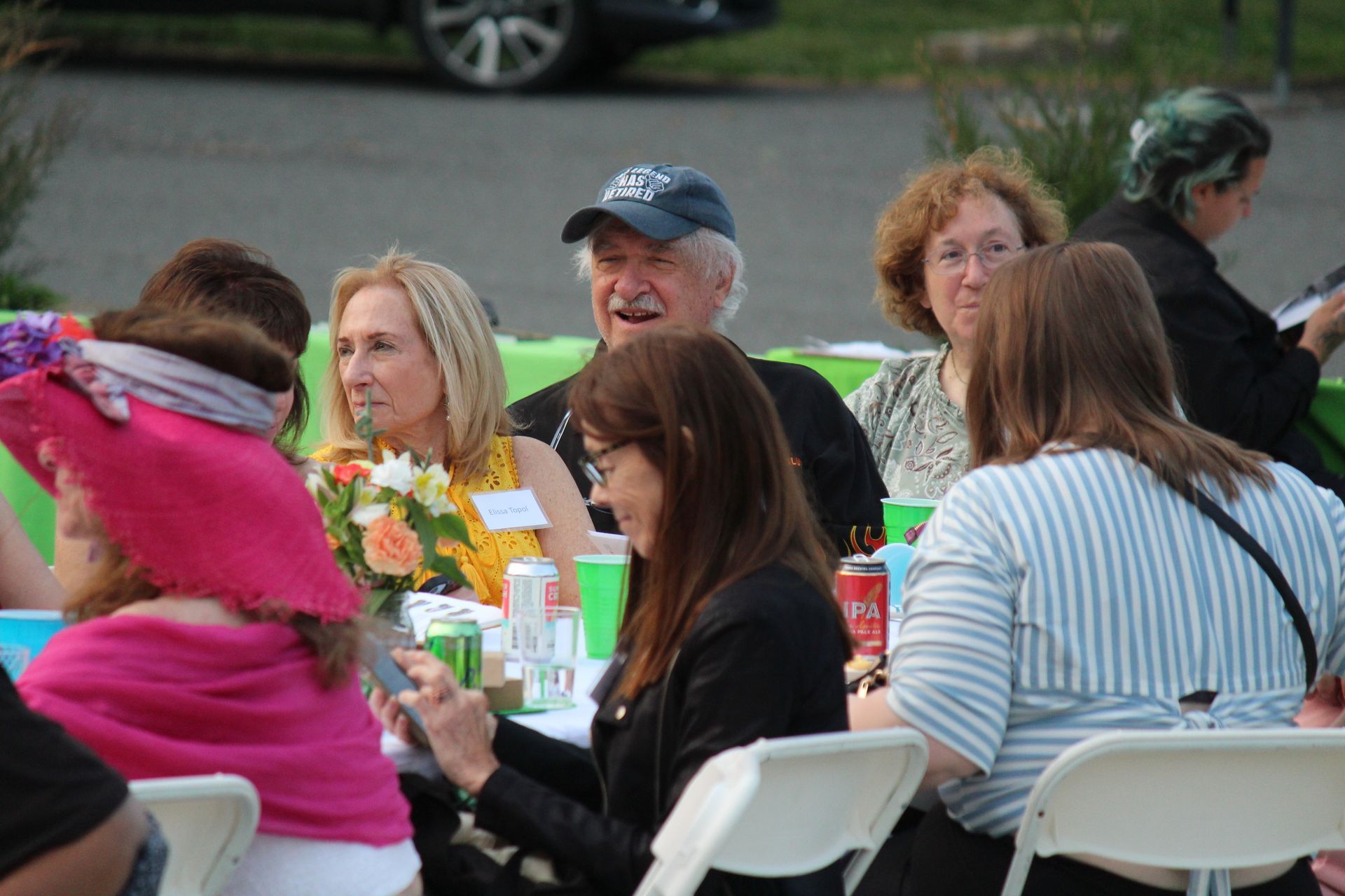 People seated at an outdoor table with drinks, chatting during a casual gathering.