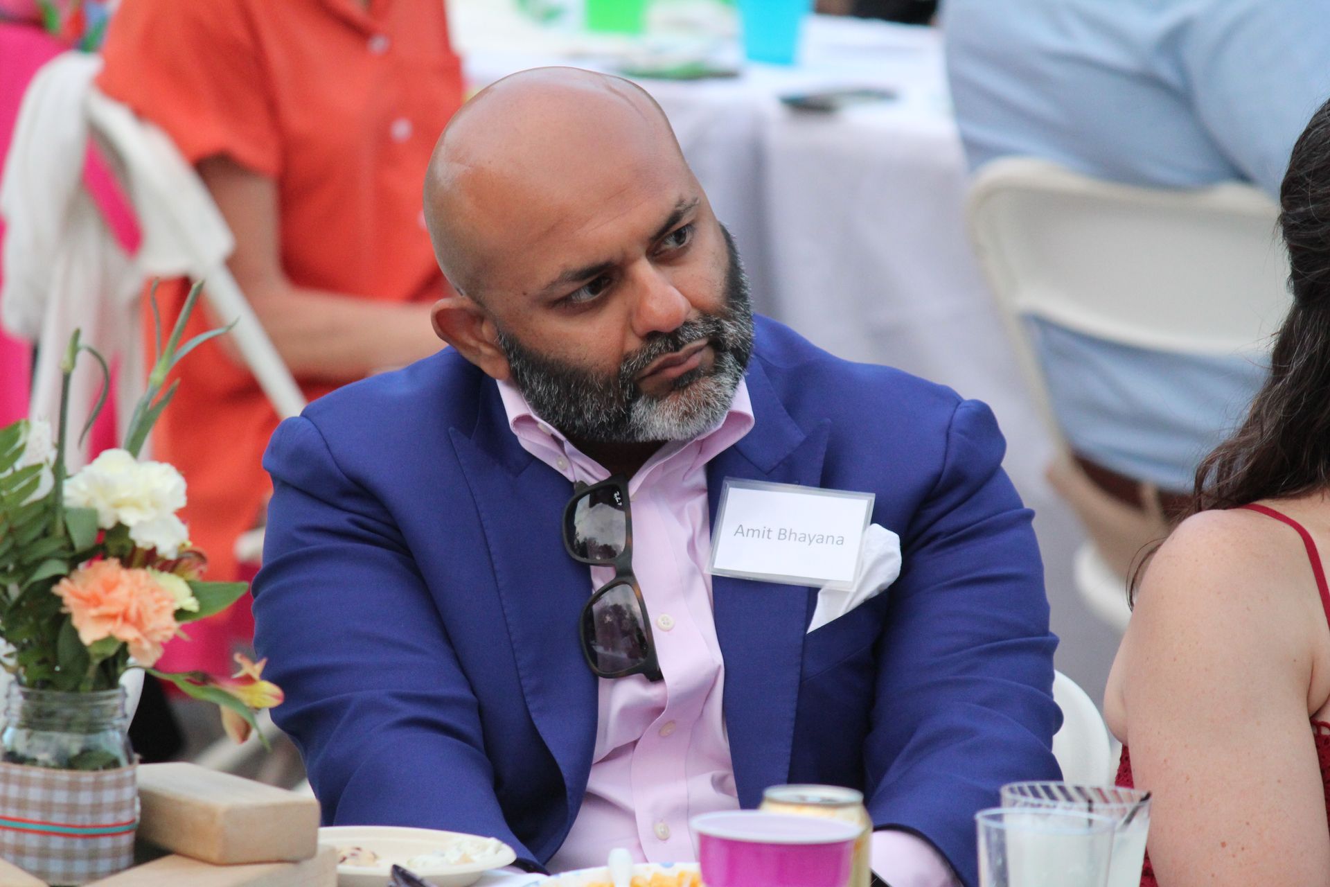 Man in a blue suit seated at a table, looking to the side at an outdoor event