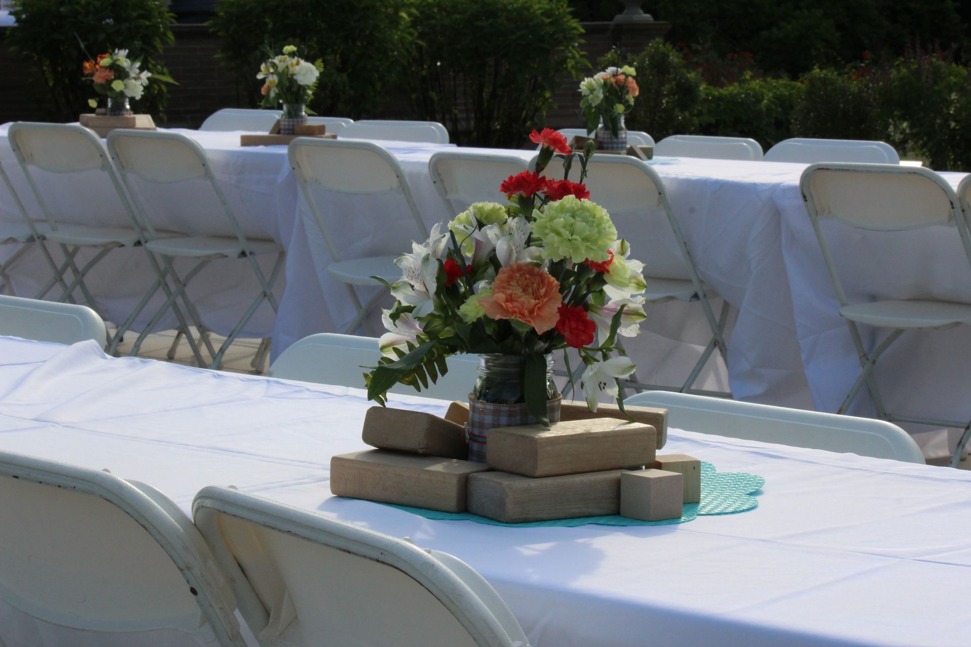 Outdoor reception tables with white linens and a small floral centerpiece on stacked books