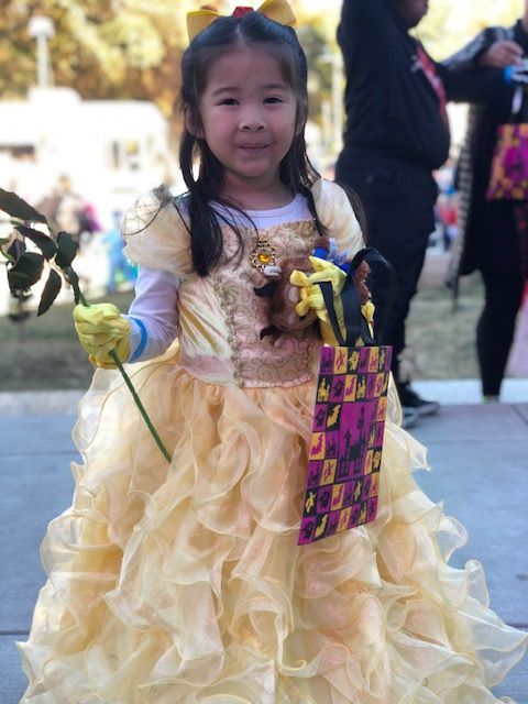 Child in a yellow princess dress holding a decorated basket, standing outdoors with a flower bouquet.