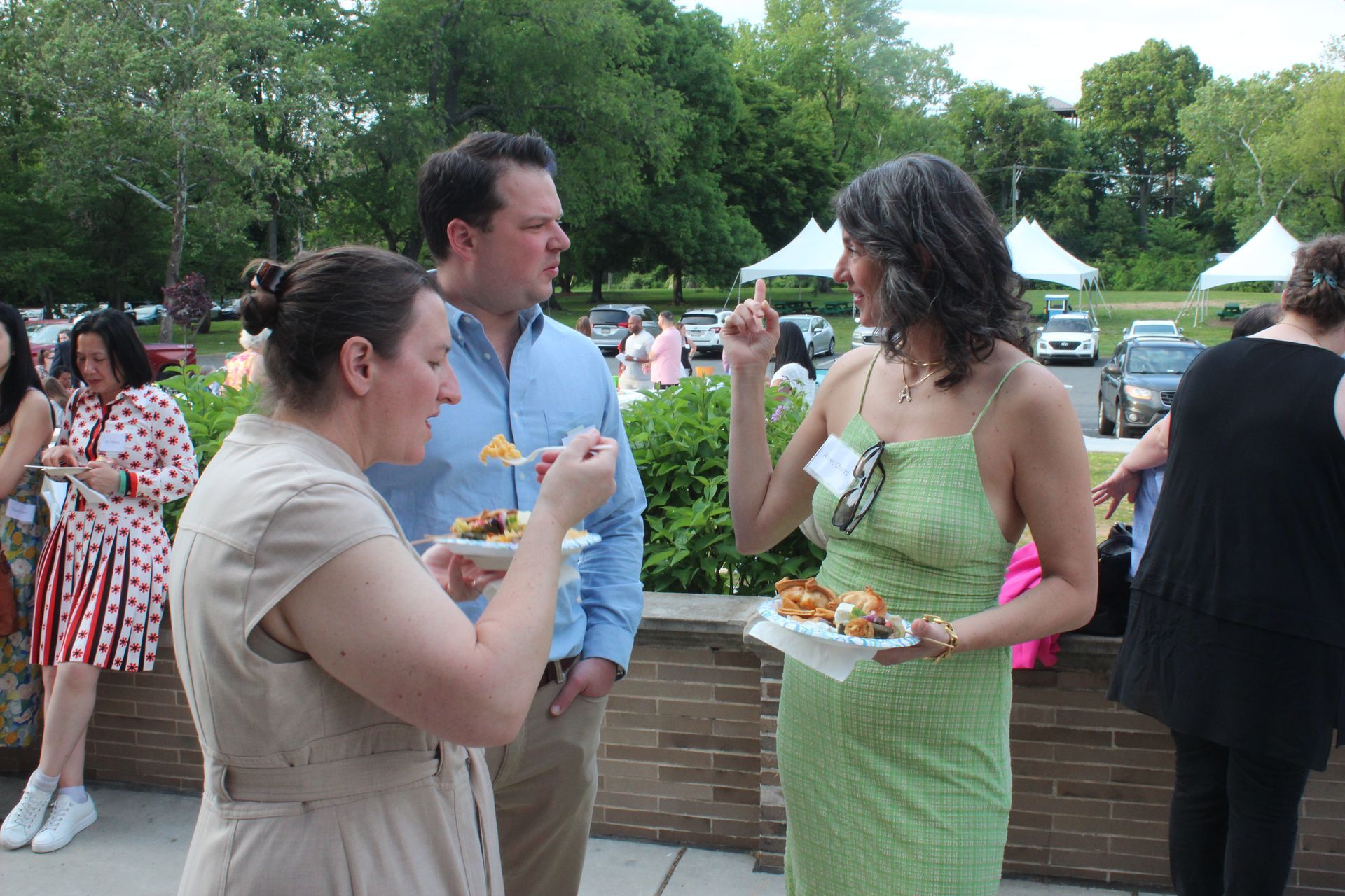 People chatting and eating at an outdoor garden gathering with tents in the background
