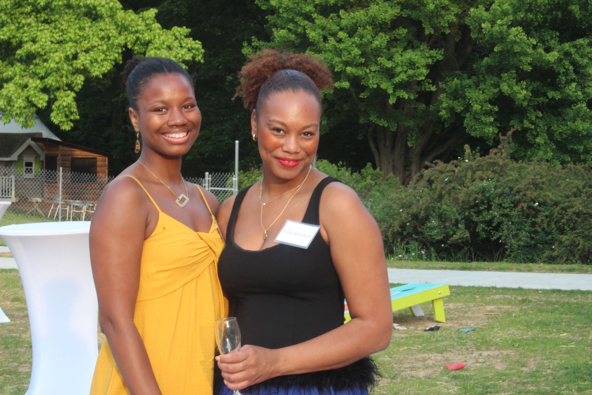 Two women smiling outdoors at a garden event, standing beside a white cocktail table.