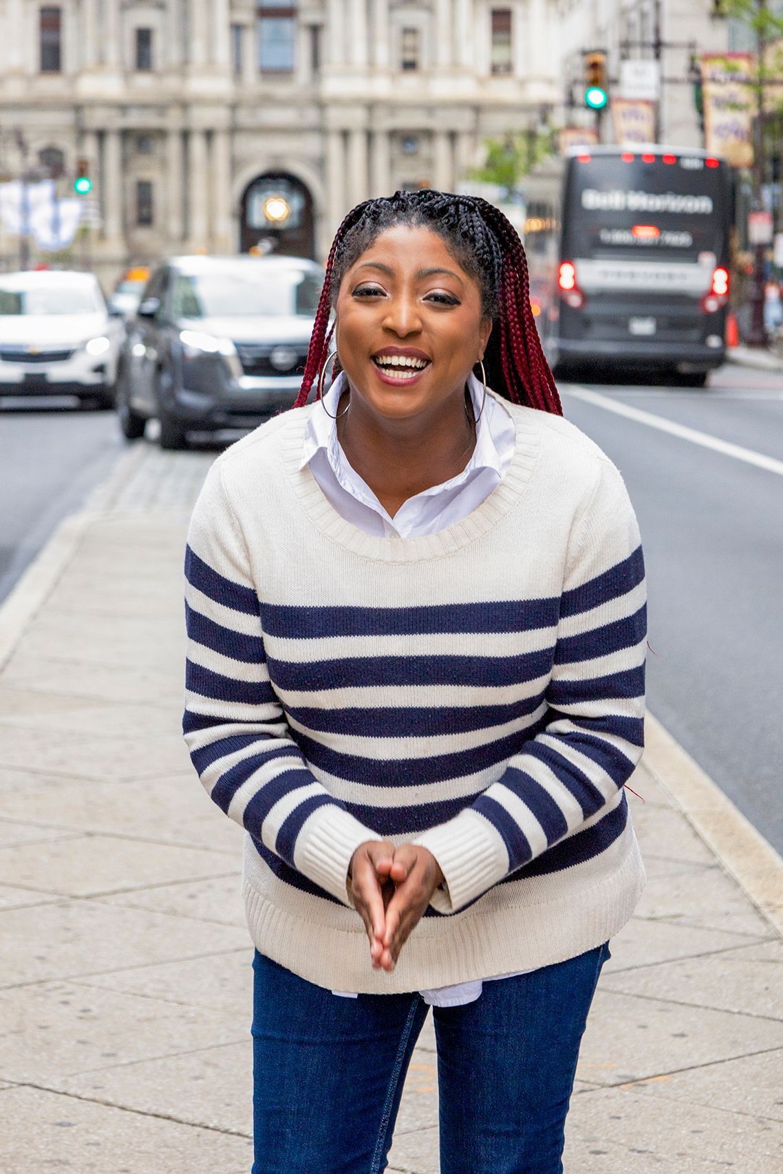 Smiling woman in a white top and beige pants standing on a city street with a blurred building behind her