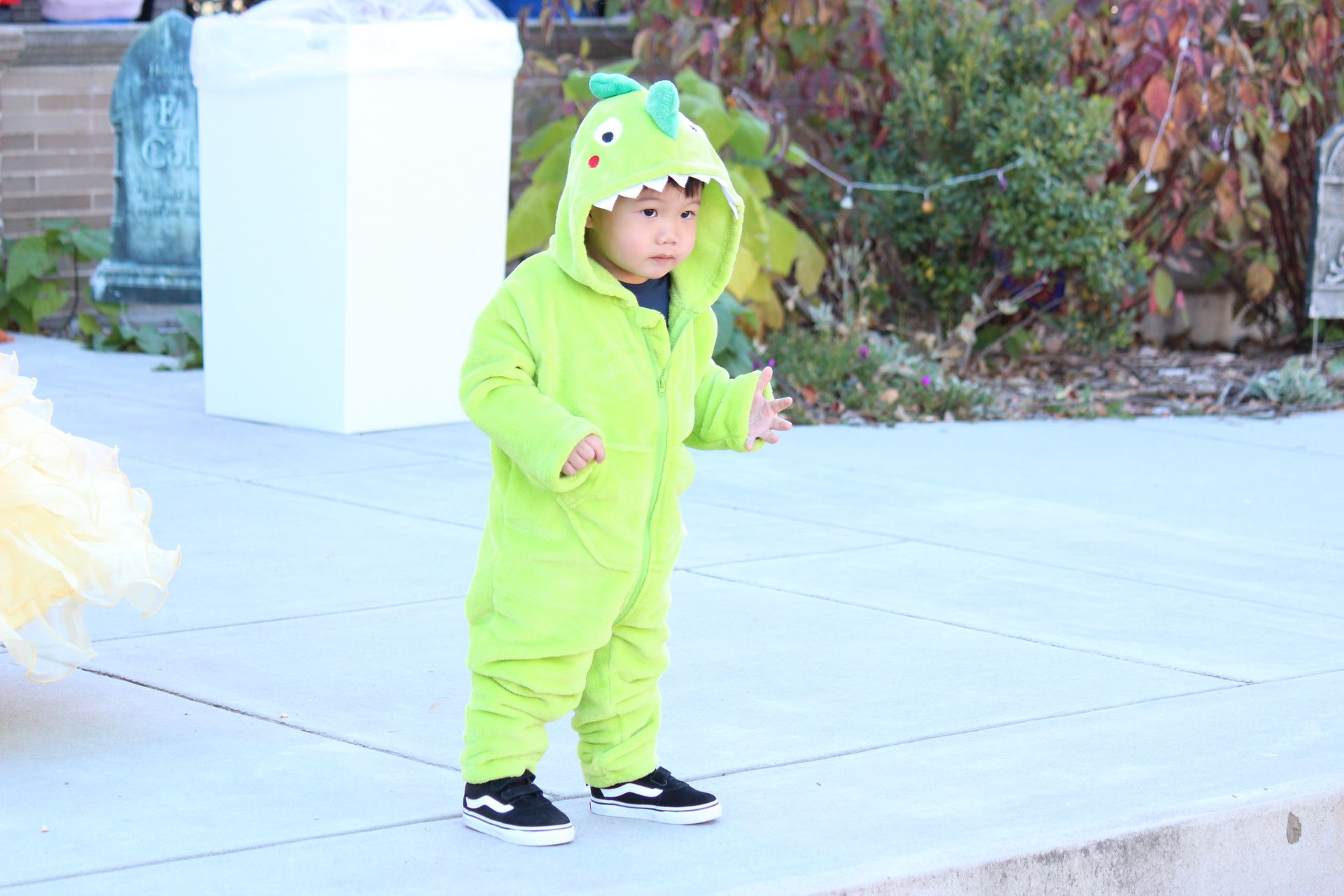 Child in bright green dinosaur costume standing on a sidewalk outdoors