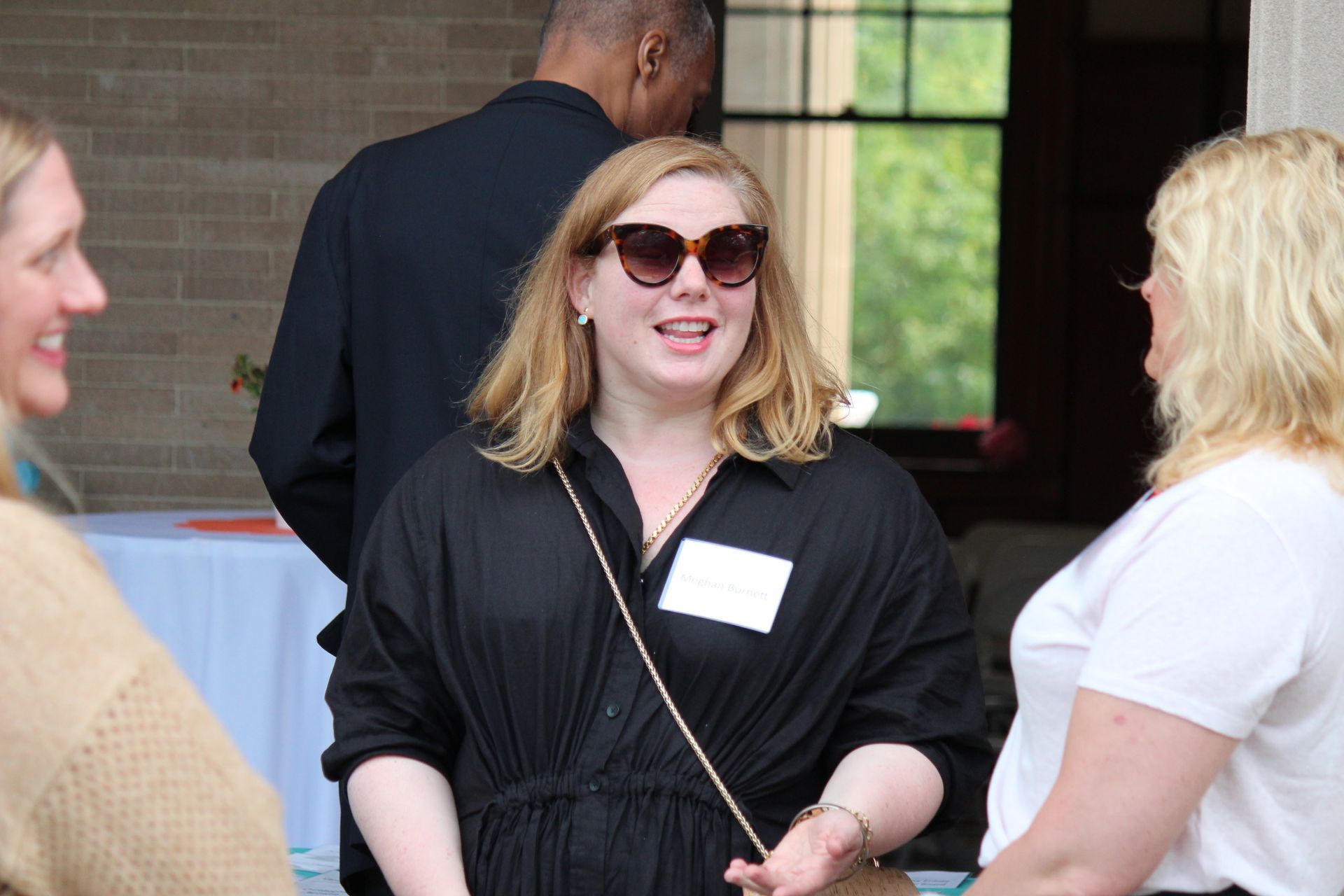 Woman in black dress and sunglasses chatting outdoors with two people at an event